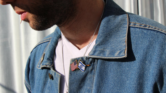 Person wearing a denim jacket with a pin featuring the american and israeli flags.