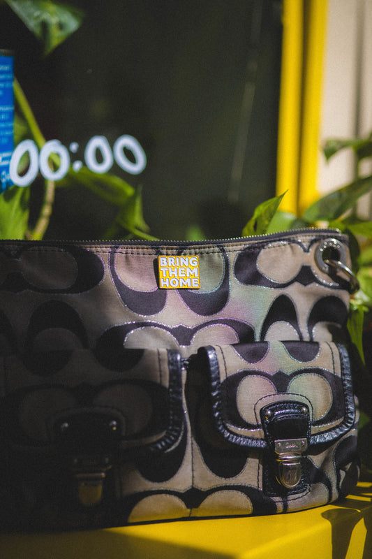 Patterned handbag with 'Bring Them Home' tag on a yellow surface