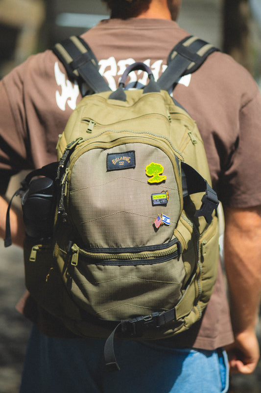 Person wearing a green backpack with patches, blurred background