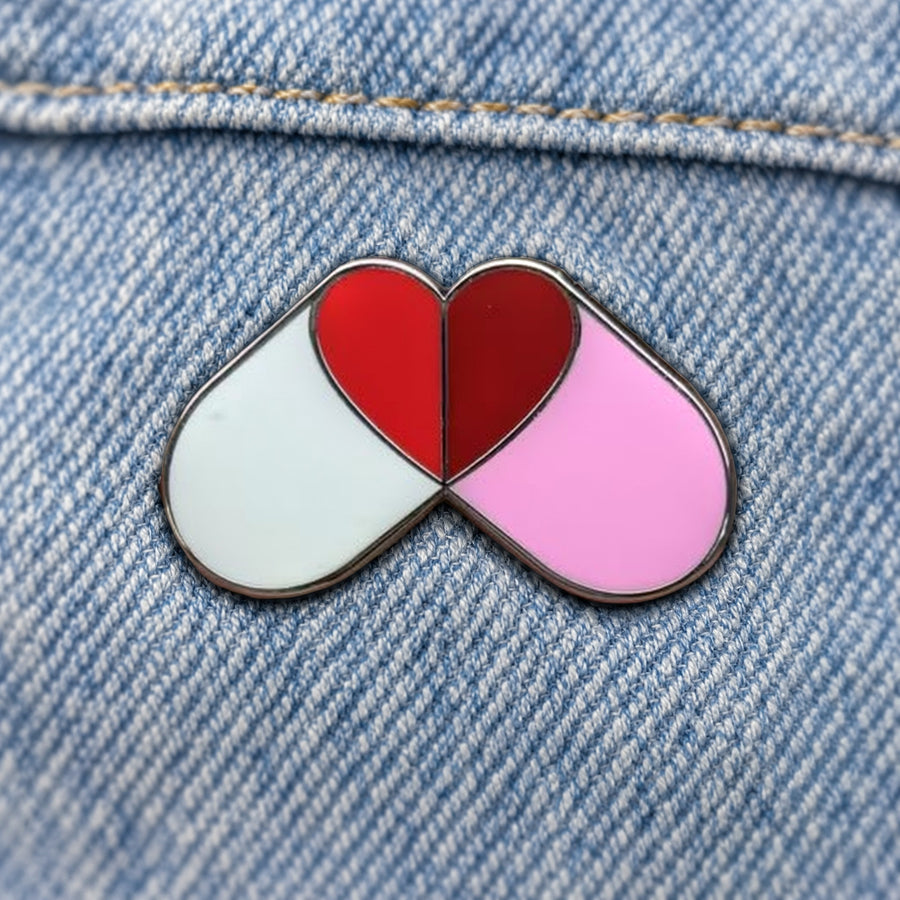 Custom enamel pin with two capsules forming a red heart on denim