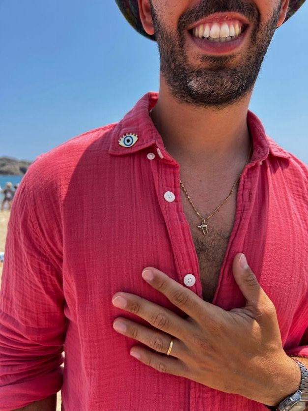 Man wearing a red shirt with a visible necklace on a beach