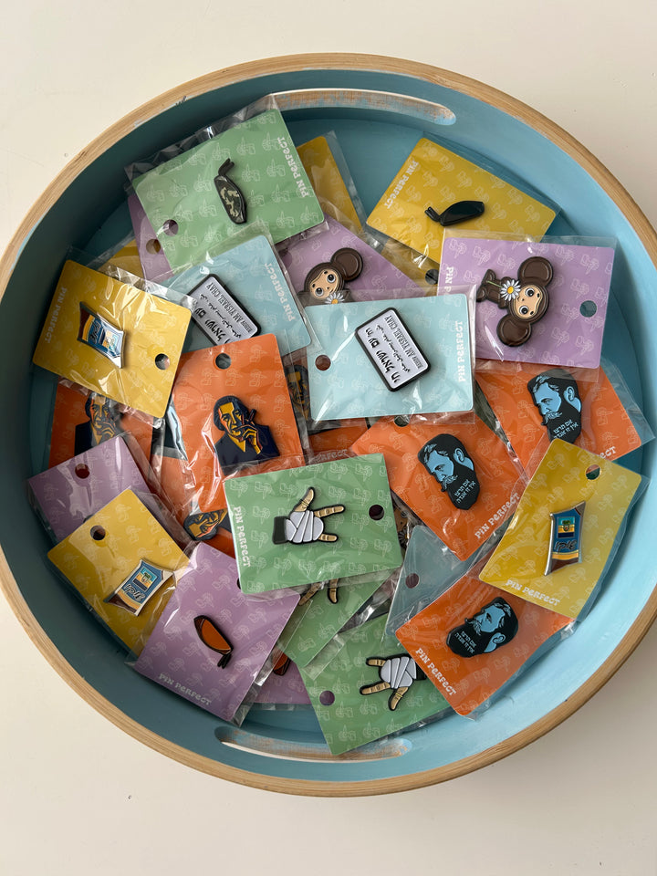 Collection of small colorful pins in packaging in a blue bowl on a white surface