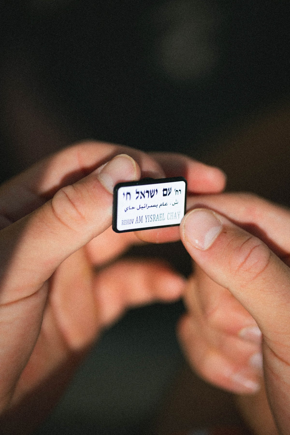hands holding an enamel pin of street sign 