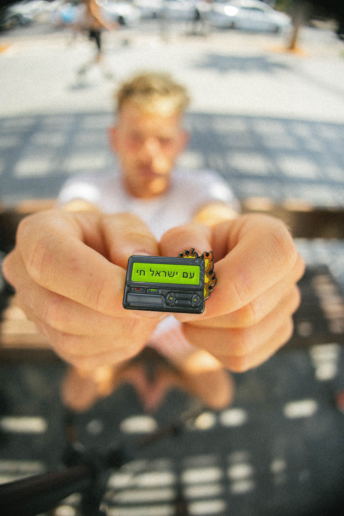 Person holding a small beeper pin with text on it, blurred background