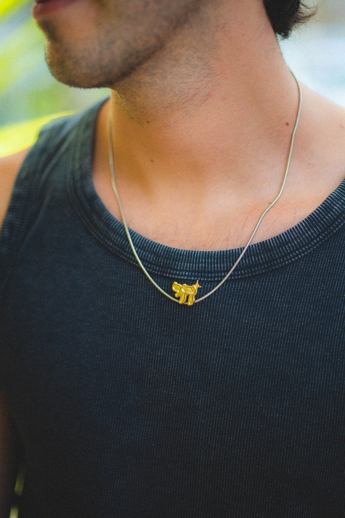 Person wearing a necklace with a small gold chai pendant outdoors