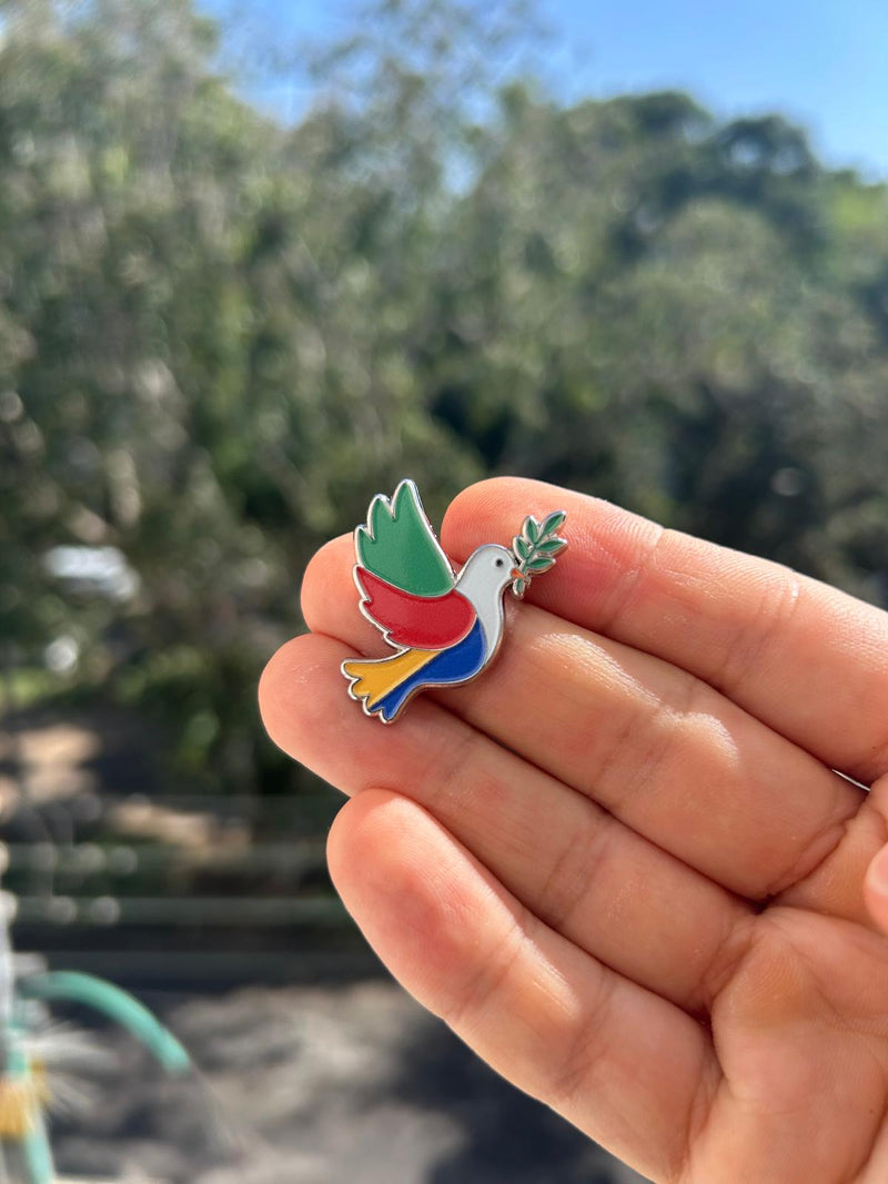Colorful dove-shaped pin held in a hand with a blurred natural background