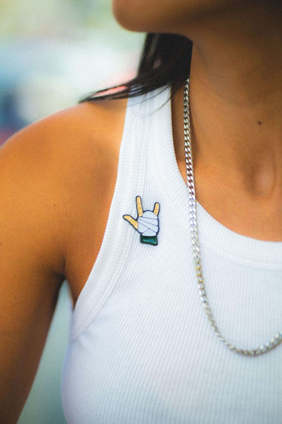 Person wearing a white tank top with a emily pin and a silver chain necklace.