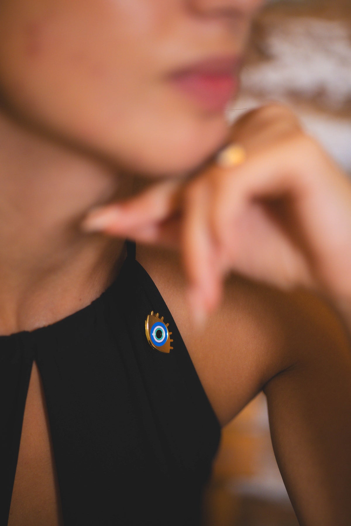 Close-up of a person wearing a black top with a gold evil eye pin.