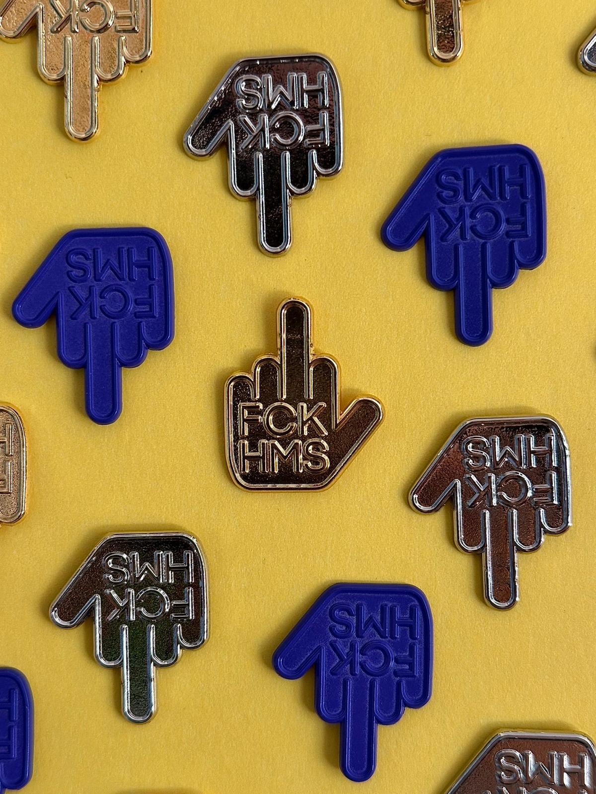 Collection of metal pins with 'FCK HMS' text on a yellow background