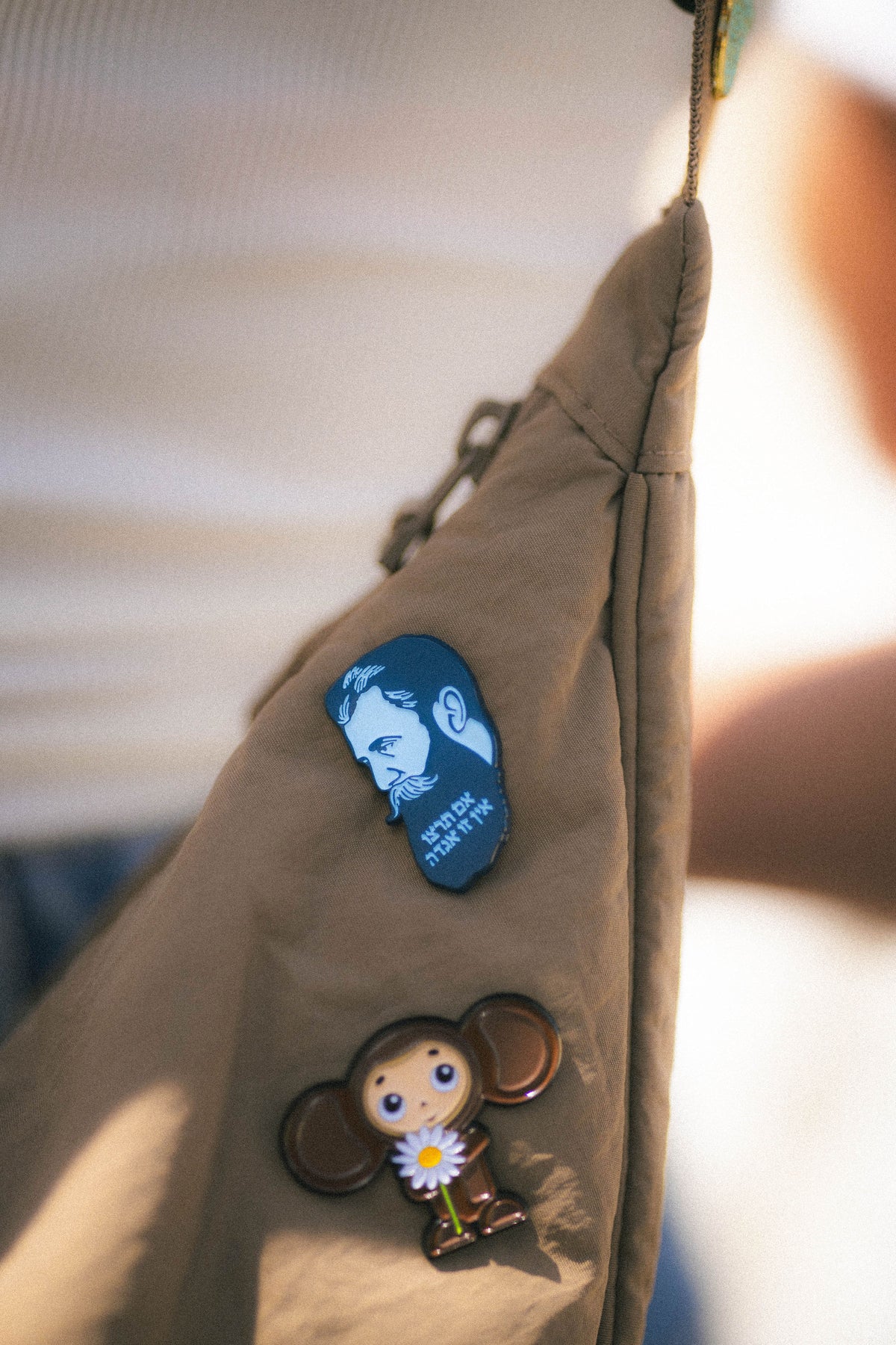 Two pins on a beige jacket, one with a cartoon character and another with a blue design.