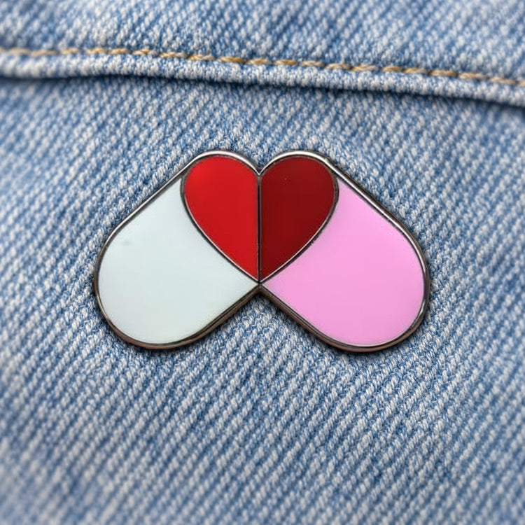Custom enamel pin with two capsules forming a red heart on denim