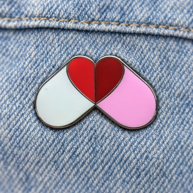 Custom enamel pin with two capsules forming a red heart on denim