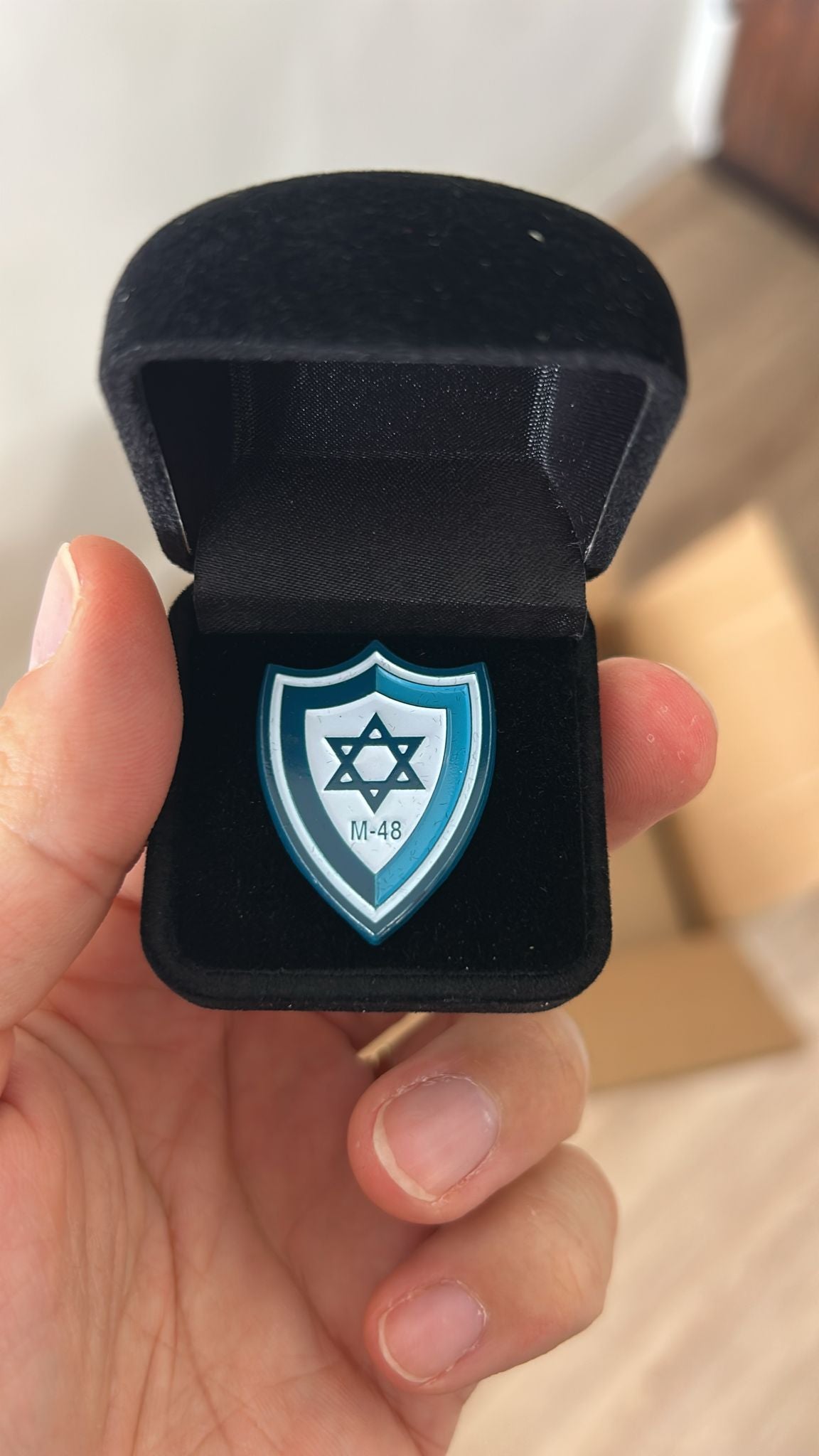 Black velvet ring box with a blue and white emblem held by a hand.