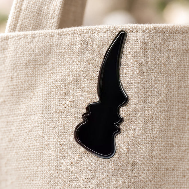Black silhouette enamel pin on a cream canvas bag