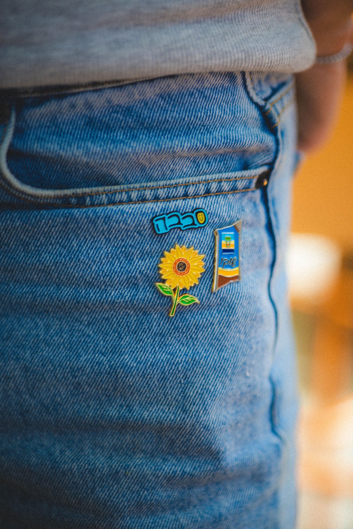 Close-up of blue jeans with a sunflower, sababa and shoko pins on the pocket.