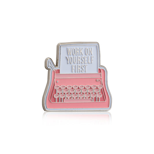 Enamel pin shaped like a typewriter with 'Work on Yourself First' text on a white background